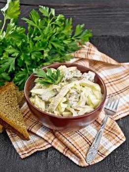 Salad with squid, egg and mushrooms in a bowl on a kitchen towel, bread, fork and parsley on wooden board background
