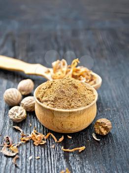 Ground nutmeg in a bowl, dried nutmeg arillus in a spoon, whole nuts on black wooden board background