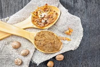 Ground nutmeg and dried nutmeg arillus in two spoons, whole nuts on burlap on a wooden board background from above