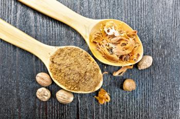 Ground nutmeg and dried nutmeg arillus in two spoons, whole nuts on a wooden board background from above