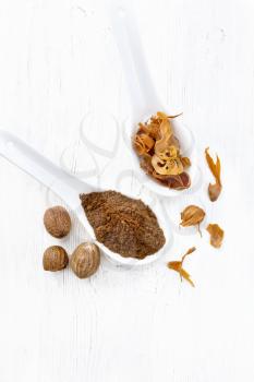 Ground nutmeg and dried nutmeg arillus  in two spoons, whole nuts on a white wooden board background from above