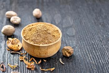 Ground nutmeg in a bowl, dried nutmeg arillus and whole nuts on a wooden board background