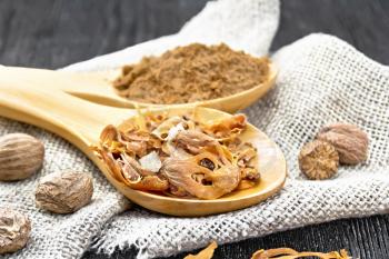 Dried nutmeg arillus and ground nutmeg in two spoons, whole nuts on burlap on a wooden board background