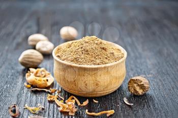 Ground nutmeg in a bowl, whole nuts and dried nutmeg arillus on a wooden board background