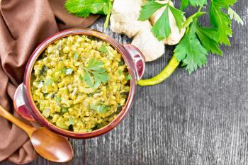 Indian national dish of kichari of mung bean, rice, celery, spinach, hot pepper and spices in a bowl on a napkin, ginger and spoon on dark wooden board background from above
