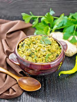 Indian national dish of kichari of mung bean, rice, celery, spinach, hot pepper and spices in a bowl on a napkin, ginger and spoon on wooden board background