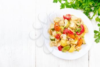 Vegetable ragout with zucchini, cabbage, potatoes, tomatoes and bell peppers in creamy sauce in plate, napkin, parsley and fork on wooden board background from above