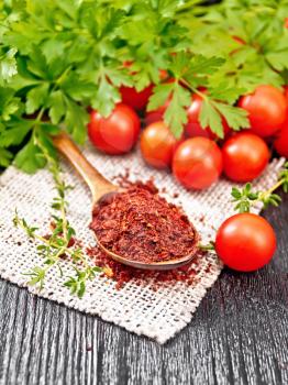 Dried tomato flakes in a spoon on burlap, fresh small tomatoes, parsley and thyme on wooden board background