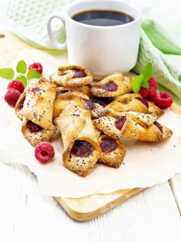 Cookies with raspberry jam, berries and mint on parchment on a plank, a cup of coffee and napkin on the background of light wooden board