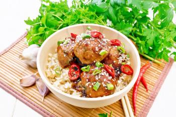 Spicy Korean meatballs in sauce of starch, soy sauce, vinegar and apricot jam, sprinkled with green onions, hot peppers and sesame seeds in a bowl on a napkin against wooden board background