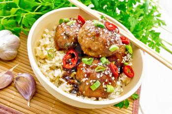 Spicy Korean meatballs in sauce of starch, soy sauce, vinegar and apricot jam, sprinkled with green onions, hot peppers and sesame seeds in a bowl on a bamboo napkin against white wooden board background