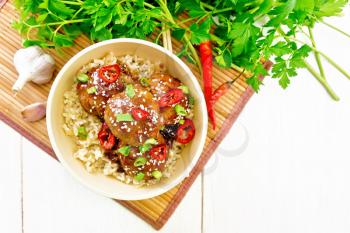 Spicy Korean meatballs in sauce of starch, soy sauce, vinegar and apricot jam sprinkled with green onions, hot peppers and sesame seeds in a bowl on a bamboo napkin against wooden board background from above