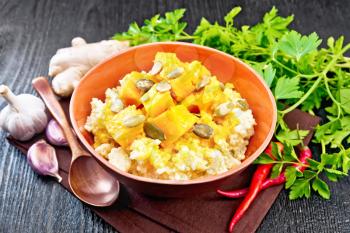 Millet porridge with spicy pumpkin sauce and seeds in a clay bowl on a towel, hot pepper, ginger root, garlic and parsley on wooden board background