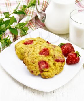 Strawberry scones in a plate with berries, a napkin, mint, milk in jug and glass on wooden board background