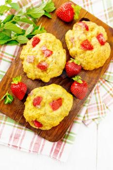 Strawberry scones with berries on a brown plate on a napkin, mint sprigs on wooden board background from above