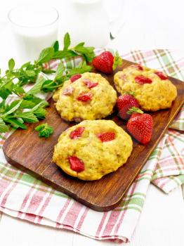 Strawberry scones with berries on a brown plate on a napkin, mint sprigs on the background of light wooden board