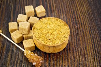 Granulated brown sugar in a bowl, crystalline on a stick and sugar cubes on wooden board background