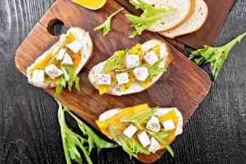 Bruschetta with baked pumpkin, salted feta cheese, ricotta, arugula and spices, napkin and vegetable slices on wooden board background from above