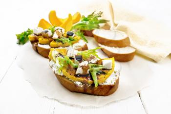 Bruschetta with baked pumpkin, salted feta cheese, ricotta, arugula, spices and balsamic sauce on parchment, napkin on wooden board background