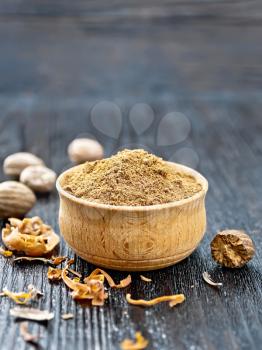 Ground nutmeg in a bowl, dried nutmeg arillus and whole nuts on a dark wooden board background