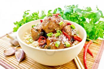 Spicy Korean meatballs in sauce of starch, soy sauce, vinegar and apricot jam, sprinkled with green onions, hot peppers and sesame seeds in a bowl on a bamboo napkin against light wooden board