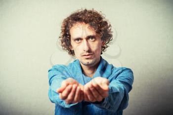 Curly young man showing empty palm. On a gray background