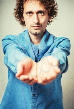 Curly young man showing empty palm. On a gray background