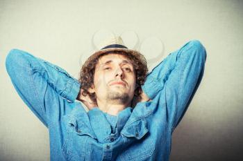 Curly young man in a wicker hat over his head put his hands resting. Back view. On a gray background