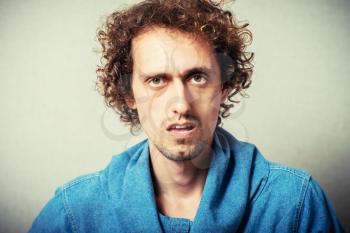 Curly young male resentment and bad mood. On a gray background