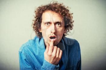 The curly-haired man finger in his mouth, a gesture of surprise. On a gray background.