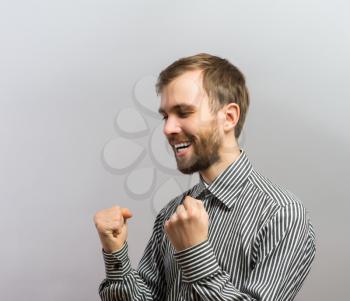 Young handsome man joyfully holding fists fan. Gesture. On a gray background