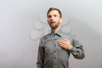Young handsome man upset hands on heart Gesture. On a gray background