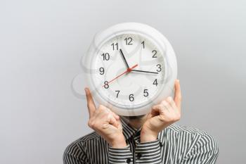 man  holding big clock covering his face over white