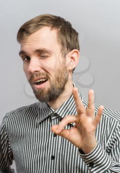 man is OK sign and close one eye while standing against grey background