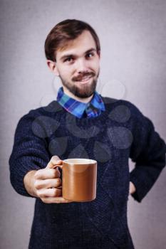 young man in a blue sweater offers a cup of tea