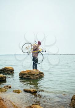 a young man with a bicycle stands on stone in lake