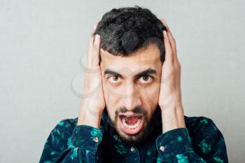 Unleashed emotions. Furious young bearded man shouting while standing against grey background