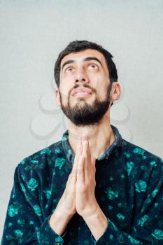 Young handsome man praying hands near your mouth. Gesture. On a gray background