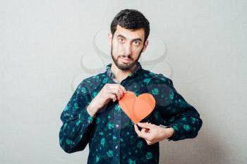 young man with beard in shirt holding red paper heart and smiling, half body