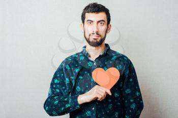 young man with beard in shirt holding red paper heart and smiling, half body