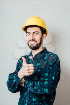 Construction worker in yellow hard hat. Happy caucasian male in his 20s. Young man portrait with thumbs up.