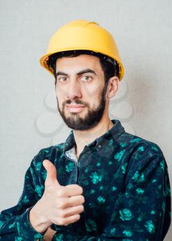 Construction worker in yellow hard hat. Happy caucasian male in his 20s. Young man portrait with thumbs up.