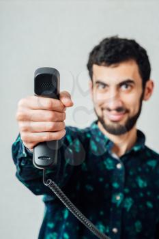 A bearded man with a phone landline, handed the phone to the camera