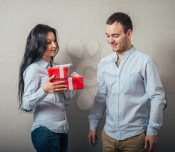 Girl is giving a gift to her boyfriend. Isolated on a gray background.