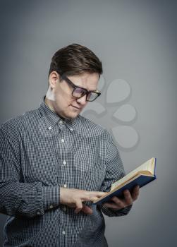Portrait of young man in glasses reading isolated over grey background