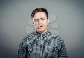 Closeup portrait, funny annoyed young childish rude bully man sticking his tongue out at you camera, isolated gray  background. Negative emotion facial expression feelings, signs, symbols