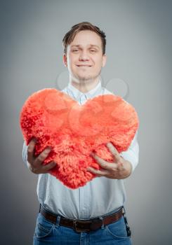 Young male holding a red heart shaped pillow and a blank banner isolated 