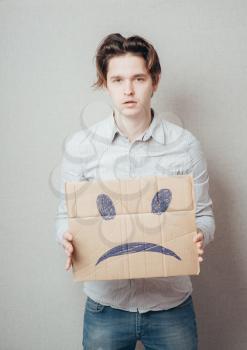 young man holding a picture of a sad smiley