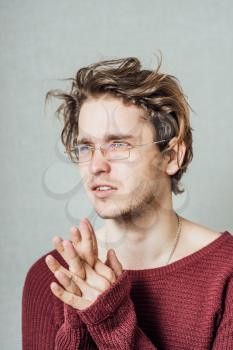 The man in glasses hands together praying. On a gray background.