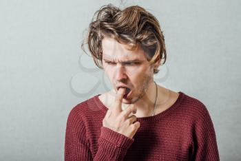 Man thinks with finger in his mouth. Gray background